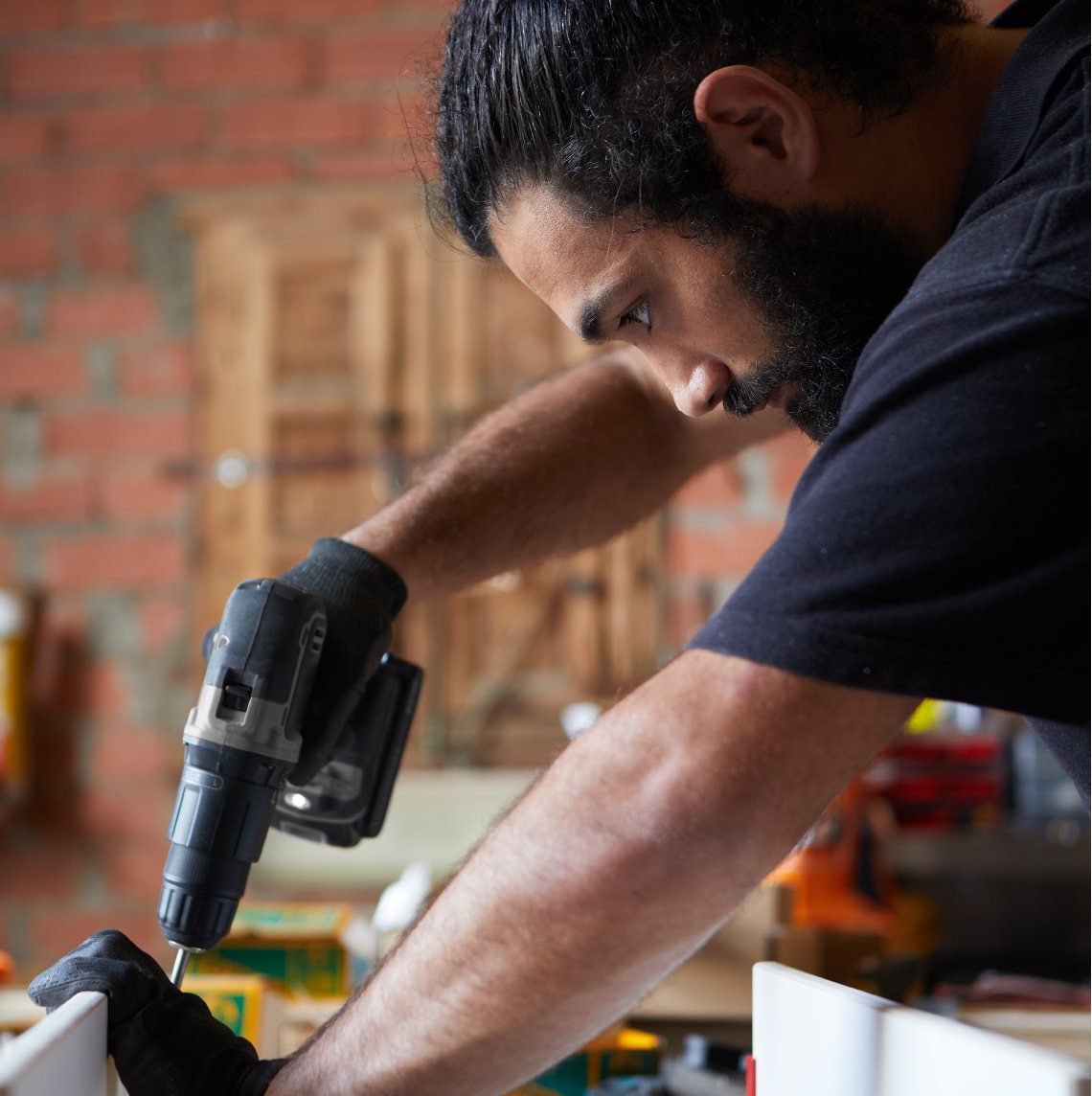 Latinx man using power drill in his workshop.